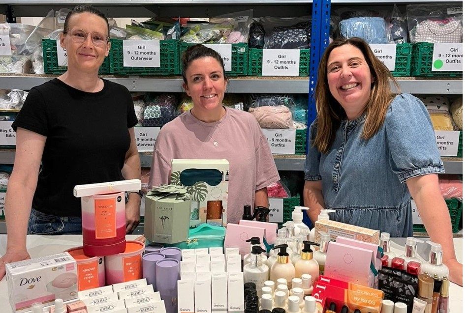 Baby Bank volunteers standing behind tables of sorted toiletries and baby essentials